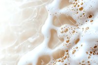 Creamy white foam with golden bubbles creating abstract pattern on light beige background, macro photography of coffee latte or beer froth texture.