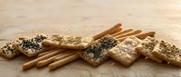 Assorted crackers and breadsticks with seeds and herbs on wooden surface for snacking, appetizers, or bakery product marketing.