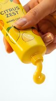 Hand holding yellow citrus zest hand care product bottle with gel dispensing, isolated on white background for skincare and cosmetics advertising.