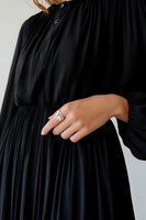Elegant black pleated dress with long sleeves shown on female model wearing gold ring. Fashion detail photograph against white background for clothing retail.