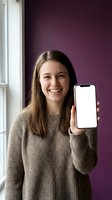 Happy young woman holding smartphone with blank white screen in modern purple interior for app presentation and mobile marketing campaigns.