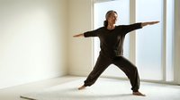 Middle-aged Caucasian woman practicing warrior yoga pose in bright modern studio with large windows. Fitness wellness meditation exercise routine.