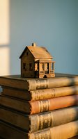 Miniature wooden house model sitting on stack of vintage leather-bound books symbolizing home education, real estate knowledge and property investment learning.