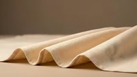 Soft beige fabric with gentle waves and folds creating elegant textile texture. Natural cotton or linen material with warm neutral tones for interior design projects.