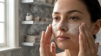Young woman applying facial cleanser with foam on face during morning skincare routine in modern bathroom with natural lighting for healthy skin care.