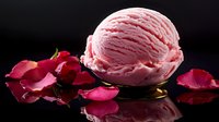 Pink rose-flavored ice cream scoop on dark reflective surface with scattered red rose petals creating romantic mood and elegant composition.