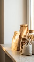 Kraft paper bags and fabric pouches with twine on marble surface near window, suitable for food packaging, product storage, and retail display purposes.