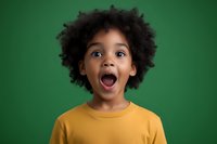 Young African American child with natural curly hair expressing pure joy and excitement while wearing yellow t-shirt against green background, capturing genuine emotion.