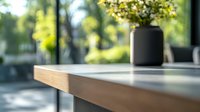Minimalist wooden table corner with black vase and flowers in sunlit room, soft bokeh background creates peaceful atmosphere for modern interior design.