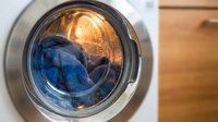 Blue denim jeans spinning inside modern washing machine drum with warm interior lighting. Laundry day household chore concept for home cleaning routines.