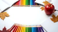 Colorful pencils arranged in rainbow spectrum with red apple and autumn leaves on white background for back to school creative projects and education.