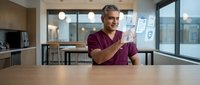 Middle-aged Hispanic male healthcare professional in burgundy scrubs using holographic digital interface technology in modern medical facility.