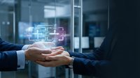 Young male and female professionals in business attire joining hands over glowing digital network icons, symbolizing teamwork, collaboration, and technology integration in corporate environment.