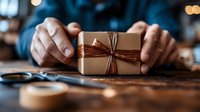 Hands protecting wrapped gift box with brown paper and twine bow on wooden table. Holiday present giving concept for Christmas celebrations and special occasions.