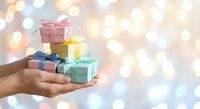 Hands holding colorful wrapped gift boxes with ribbons against soft bokeh lights background for holidays and celebrations.