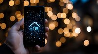 Glowing house icon on smartphone screen against blurred golden bokeh lights background, representing smart home technology and digital connectivity.