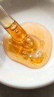 Golden honey dripping from wooden dipper into bowl with white background, suitable for food, cooking, and wellness product photography and design.