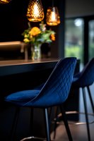 Elegant navy blue velvet bar stool with quilted pattern under warm pendant lights. Fresh flowers in vase create luxurious restaurant or home bar atmosphere.