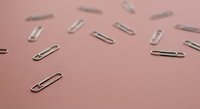 Silver metal paper clips scattered on soft pink background for office supplies and stationery organization concepts.