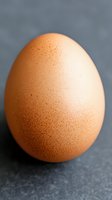 Fresh brown chicken egg with speckled shell texture on dark gray background, macro photography showing natural organic food in minimalist composition.