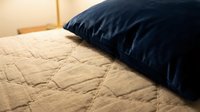 Cozy bedroom scene with navy blue velvet pillow resting on beige quilted bedding, creating a warm and inviting sleeping space for home decor and lifestyle content.