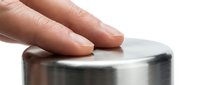 Hand touching smooth metallic surface with fingers making contact on brushed steel cylinder for tactile sensory experience and material testing.
