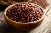Brown rice grains in wooden bowl on rustic table, close up macro shot with selective focus showing natural texture and nutritious whole grain.