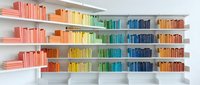 Modern home library with colorful books arranged by rainbow spectrum on white floating shelves creating organized minimalist interior design aesthetic.