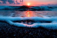 Ocean waves washing onto pebble beach at sunset with dramatic sky and golden light reflecting on water creating peaceful seascape atmosphere.