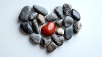 Heart shape made of gray and black river stones with single red jasper stone in center on white background, symbolizing uniqueness and standing out from crowd.