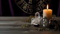 Mystical altar setup with burning candle, pentagram pendant, crystal quartz and dried herbs on wooden table with zodiac wheel background for spiritual practices.
