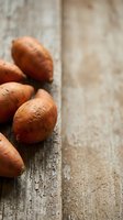 Fresh russet potatoes arranged on weathered wooden surface with neutral background, suitable for food photography, culinary content, and cooking-related projects.