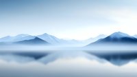 Tranquil mountain lake landscape with perfect mirror reflection in calm water, layered blue peaks shrouded in morning mist creating ethereal atmosphere.