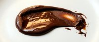 Melted chocolate spread on white surface with glossy, flowing texture and rich brown tones, suitable for food photography, culinary content, and dessert marketing materials.