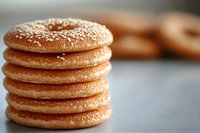 Stack of fresh sesame bagels with golden crust and white seeds on blurred background, selective focus on crispy bread surface. Perfect for food blogs and menus.