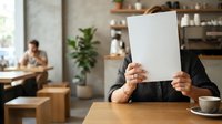 Businesswoman holding blank white paper in modern office workspace with colleagues working in background, suitable for corporate communications and business messaging concepts.