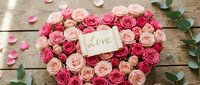 Heart-shaped arrangement of pink roses with a love note card on rustic wooden background, perfect for Valentine's Day and romantic celebrations.
