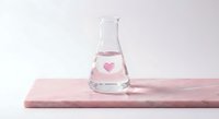 Glass laboratory flask with pink heart symbol on marble surface for chemistry love concept and scientific romance themes.