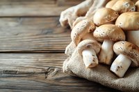 Fresh brown champignon mushrooms on rustic burlap cloth against wooden table background, selective focus with copy space for food photography.