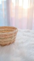 Empty wicker basket on soft white fur surface with dreamy pastel curtain background for home decor and storage concepts.
