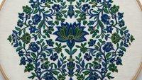 Intricate floral embroidery hoop with blue and green botanical motifs on cream fabric. Traditional needlework craft featuring symmetrical design for home decor projects.
