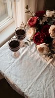 Romantic table setting with red wine glasses and elegant rose bouquet by window creating intimate atmosphere for date night or anniversary celebration.