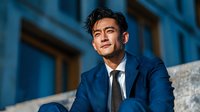 Professional Asian businessman in navy suit smiling confidently outdoors against modern building architecture during golden hour lighting for corporate success.