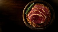 Raw ribeye steak with peppercorn crust and fresh rosemary on rustic wooden plate against dark background, dramatic food photography lighting.