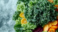 Fresh curly kale leaves with colorful raw vegetables including carrots, beets and citrus arranged on dark background. Healthy organic produce for cooking.