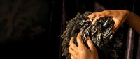 Young African American woman with natural curly hair applying shampoo during hair washing routine in shower with warm lighting and water droplets.