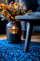Glowing candle and bokeh lights create cozy atmosphere on blue knitted carpet. Dark moody interior with warm orange highlights and selective focus.