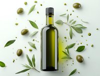 Glass bottle of extra virgin olive oil surrounded by fresh green olives and scattered olive leaves on white background, food photography composition.