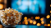 Fresh popcorn in glass bowl against blurred cinema screen and bokeh lights, creating atmospheric movie night ambiance for entertainment concepts.