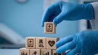 Healthcare professional in blue gloves arranging wooden blocks with medical icons representing digital health technology and telemedicine services.